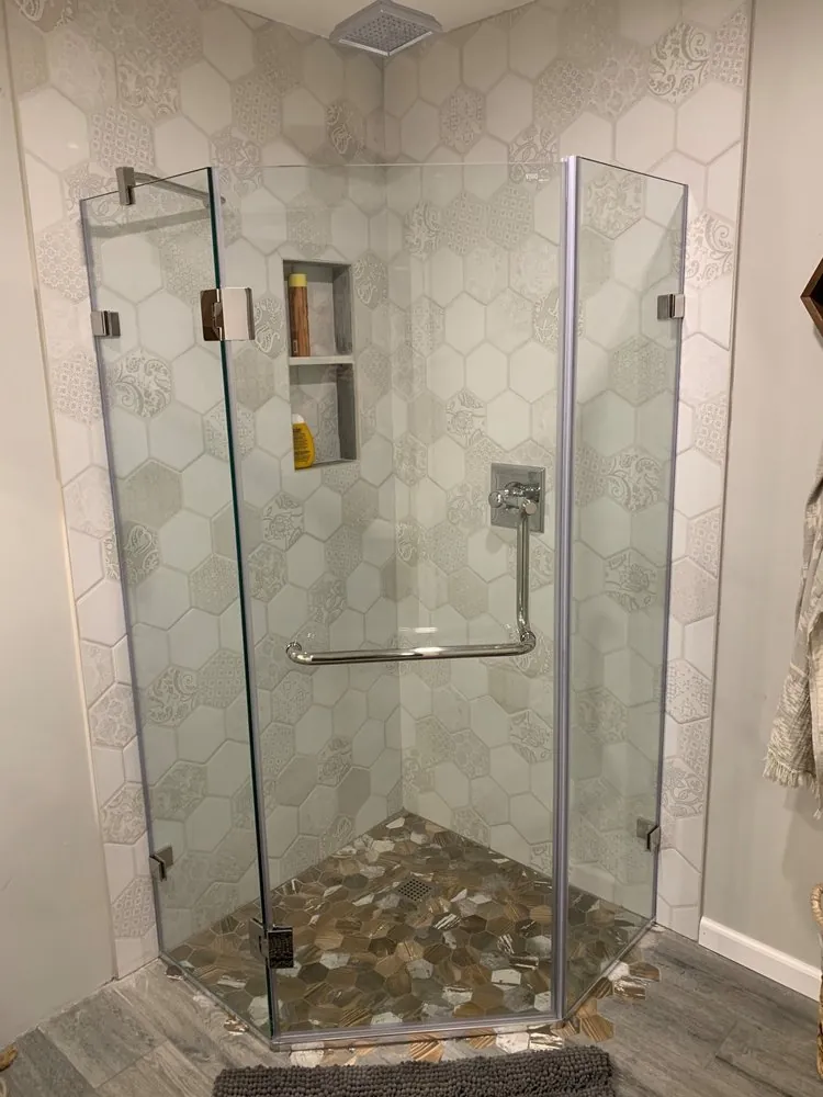 Neo-angle glass shower with white patterned hexagon wall tile, wood-look hex mosaic floor and a two-shelf niche.
