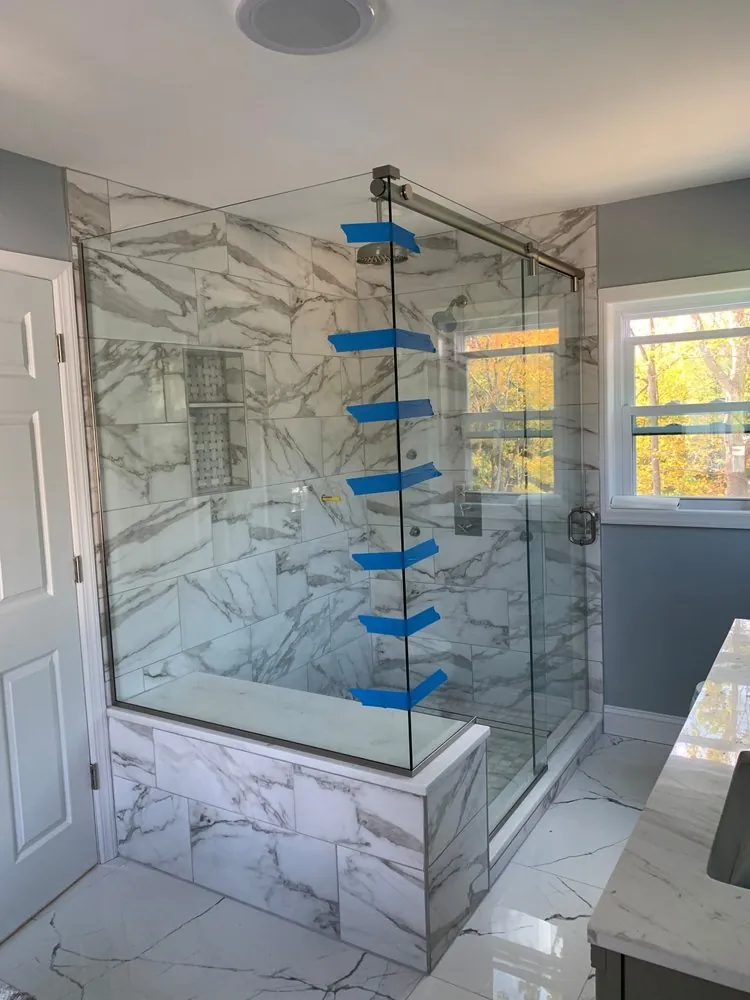Marble-look porcelain shower with built-in bench, mosaic niche and sliding glass door, glass just installed.