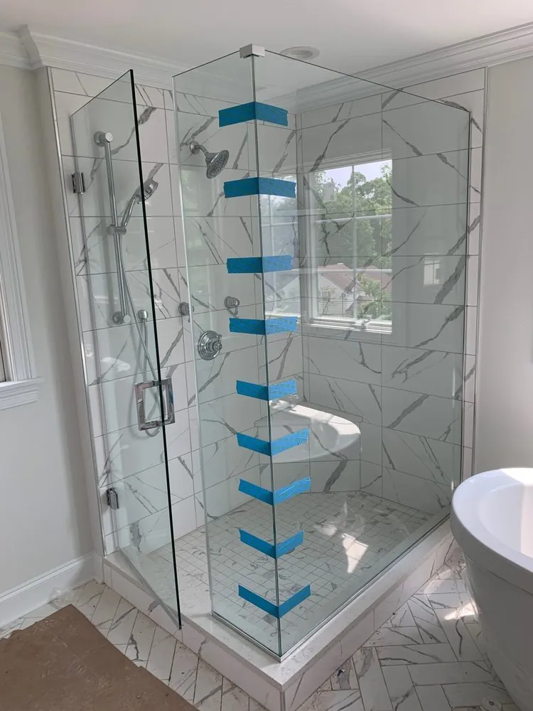 Frameless glass shower with large white marble-look porcelain tile, corner seat, window inside and chrome fixtures.