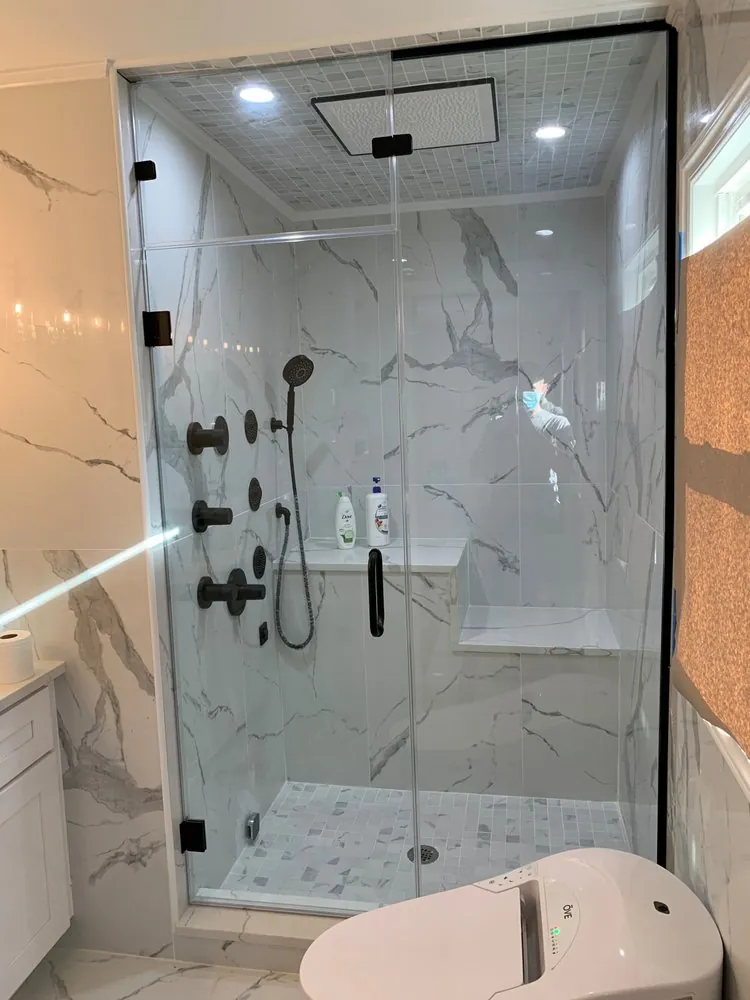Glass steam shower with white marble-look porcelain, matte black body jets and handheld, bench, mosaic floor and ceiling.
