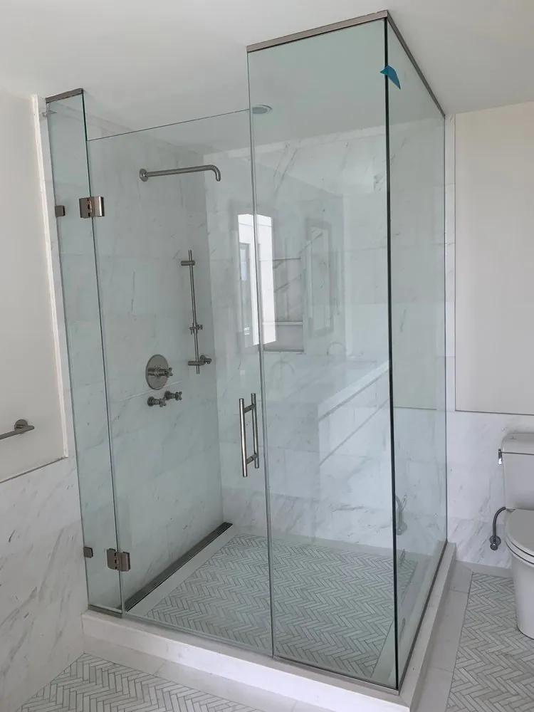 Frameless glass shower with white marble wall tile, marble herringbone floor, linear drain and brushed nickel fixtures.