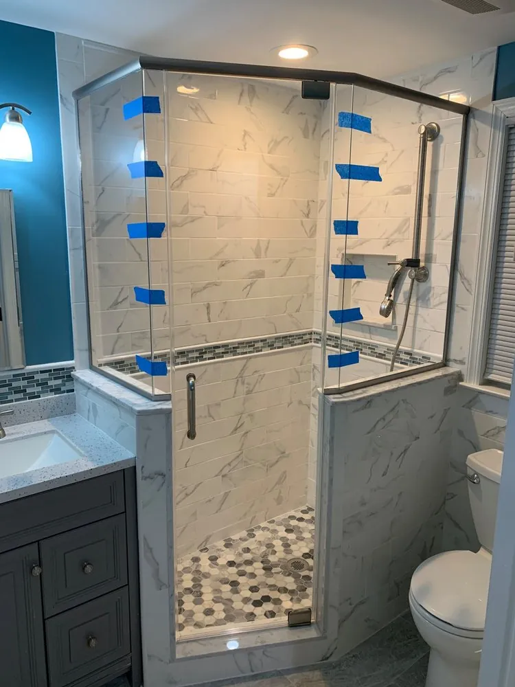 Neo-angle glass shower with white marble-look subway tile, gray mosaic band, hex mosaic floor and a gray vanity.