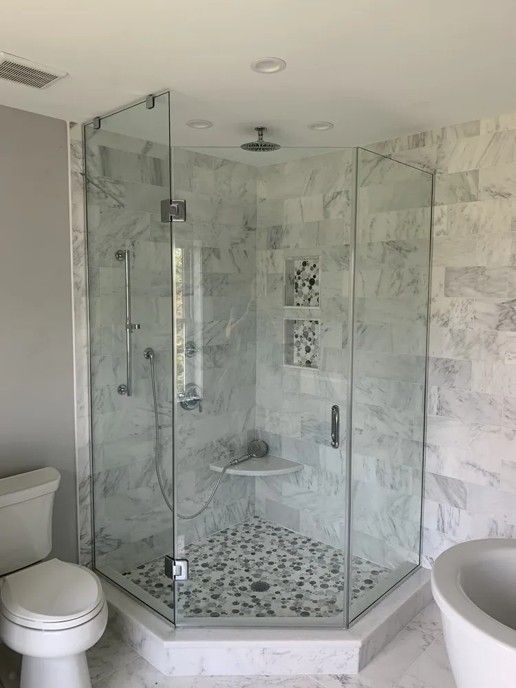 Neo-angle frameless shower with white marble subway tile, pebble mosaic floor and niches, corner seat and rain head.