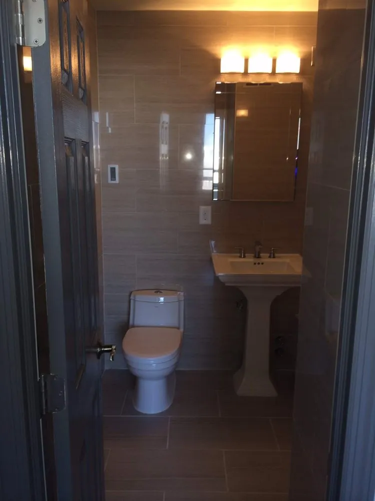 Small bathroom with taupe porcelain wall and floor tile, pedestal sink, one-piece toilet and medicine cabinet.
