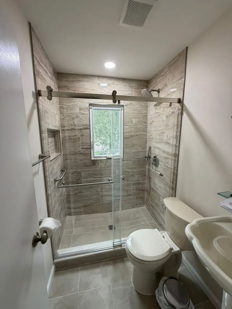 Shower with beige stone-look tile around a window, a niche, grab bars and brushed nickel sliding glass door.