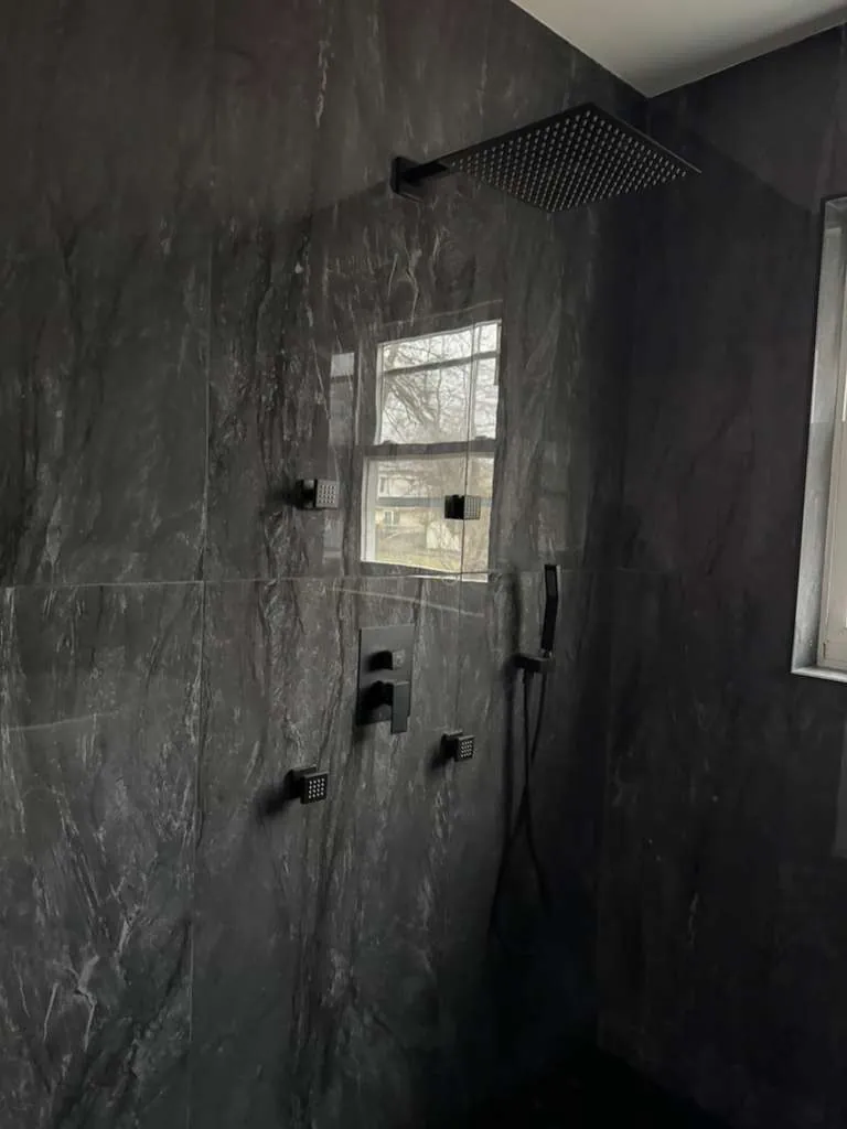Shower walls of large dark gray marble-look panels with a square rain head, body jets and matte black handheld.