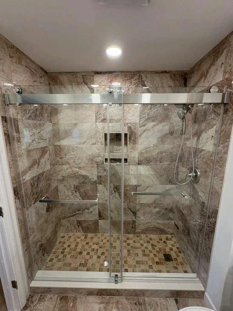 Walk-in shower with brown marble-look wall tile, tan mosaic floor, a niche, grab bars and brushed nickel sliding glass door.