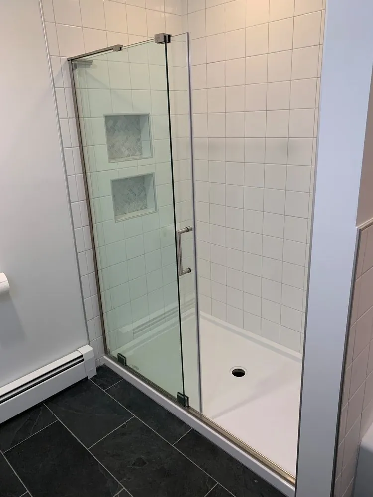 Hinged glass shower door over a white shower base, white square wall tile, two marble herringbone niches, slate floor.