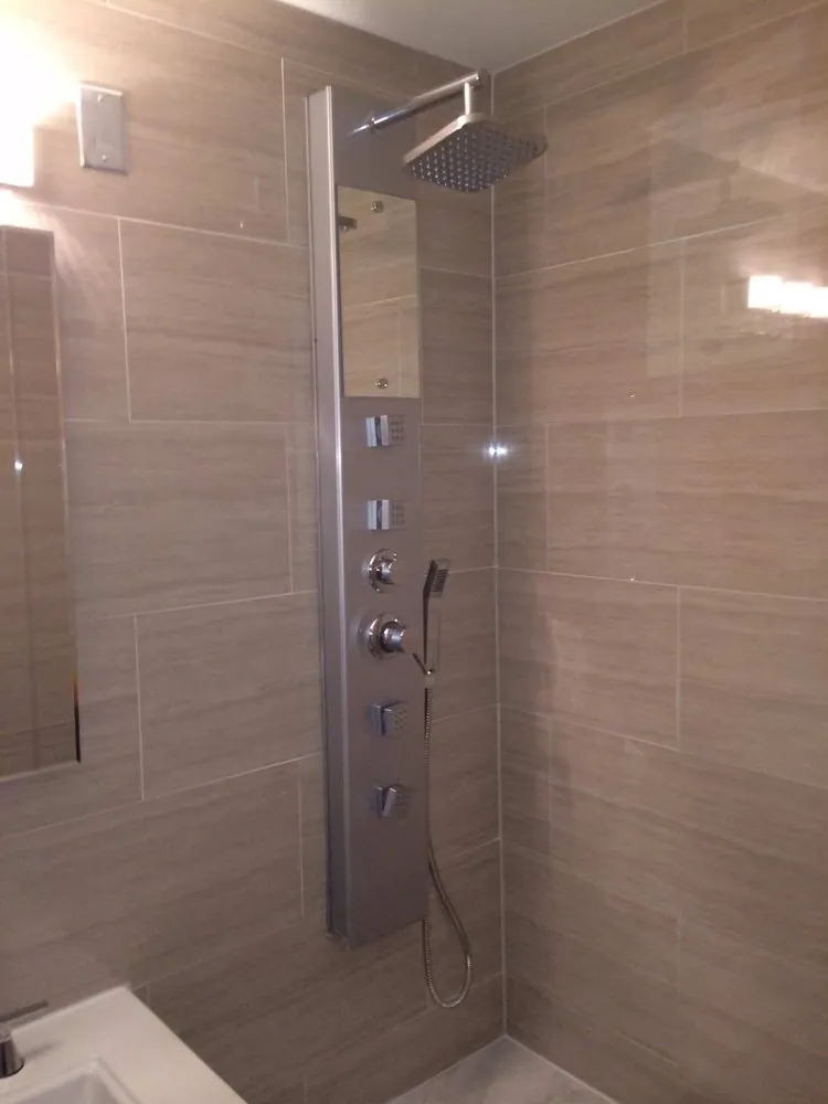 Shower with taupe linear wall tile and a brushed steel shower tower with rain head, body jets and handheld wand.