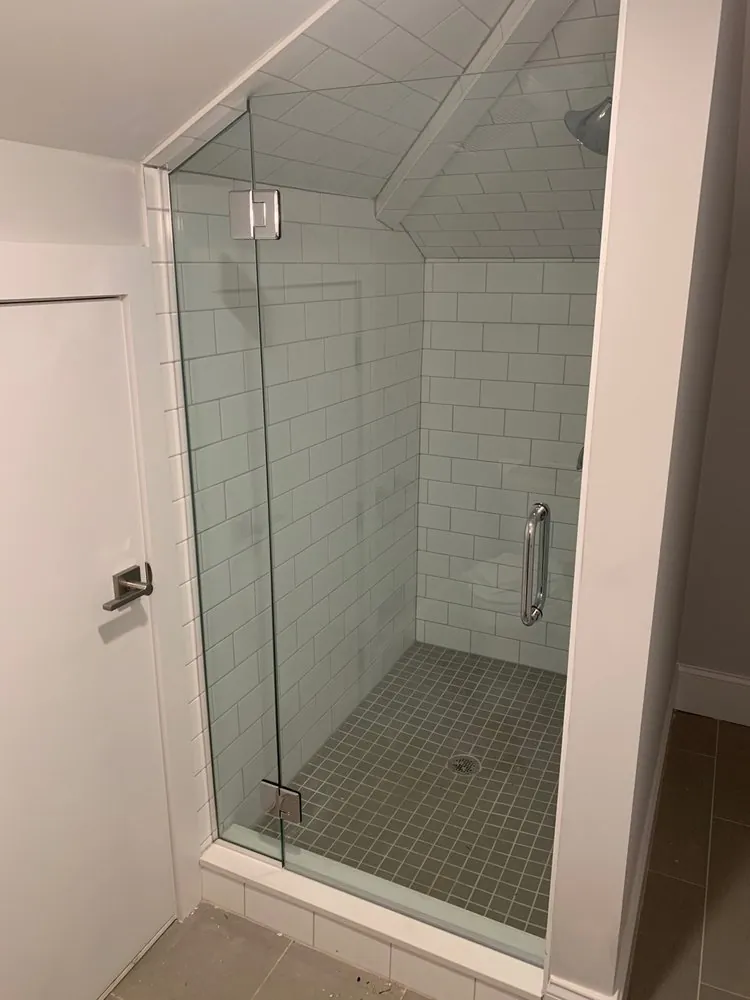 Glass shower tucked under a sloped ceiling, white subway tile on walls and ceiling, gray square mosaic floor.