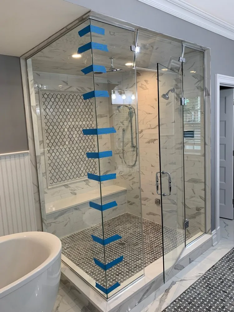 Floor-to-ceiling glass shower with white marble-look tile, framed arabesque mosaic panel, bench and basketweave floor.