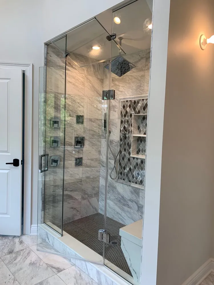 Frameless glass steam shower with gray marble-look tile, body jets, rain head and a diamond mosaic niche.