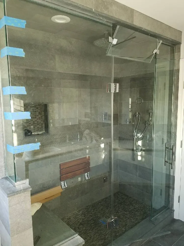 Glass steam shower with gray stone tile, mosaic niche, fold-down teak seat, rain head and handheld shower.
