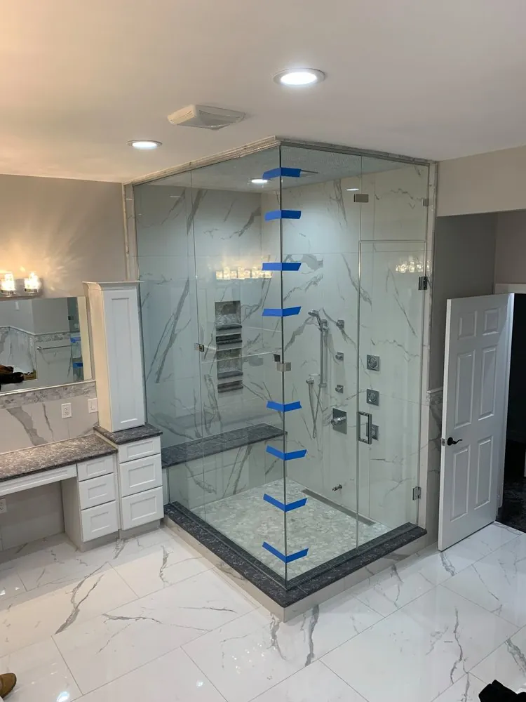 Large glass steam shower with white marble-look tile, dark granite bench and curb, body jets and a makeup vanity.