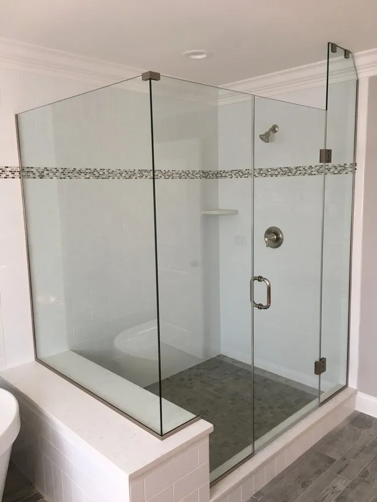 Frameless glass shower on a quartz-capped bench wall, white subway tile with mosaic band and gray mosaic floor.