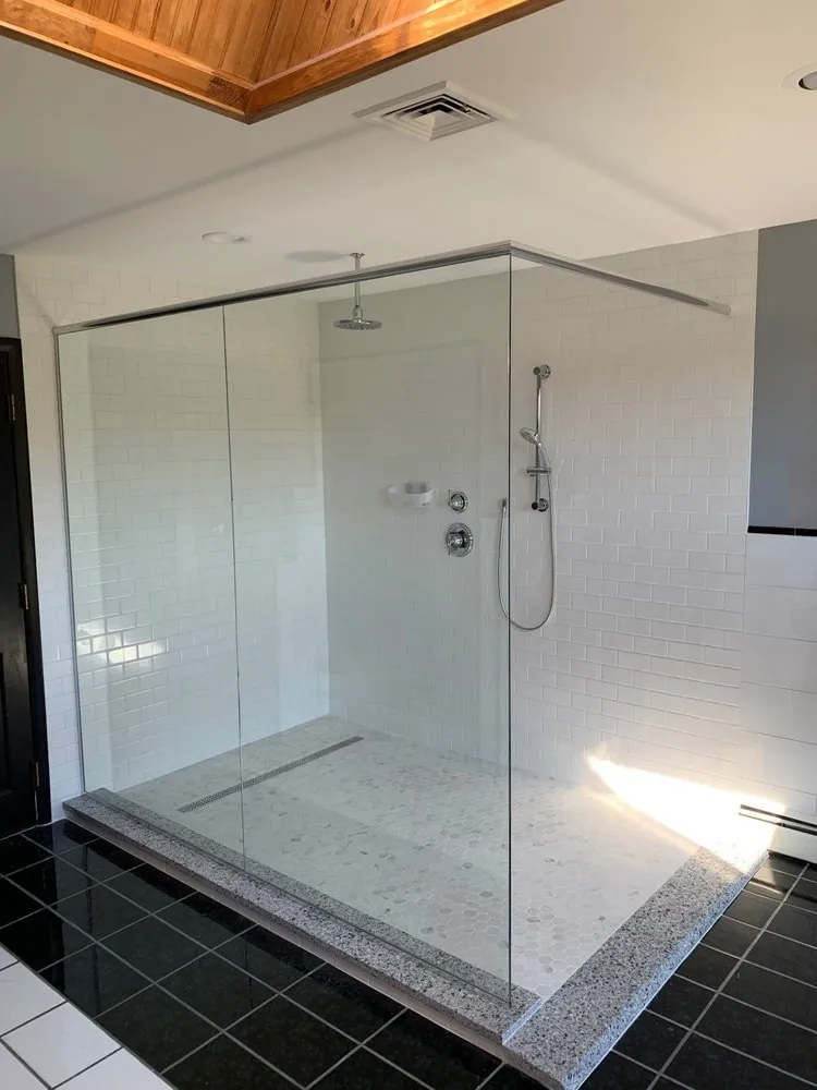 Large walk-in shower with white subway tile, marble hexagon floor, linear drain and granite curb on black tile floor.