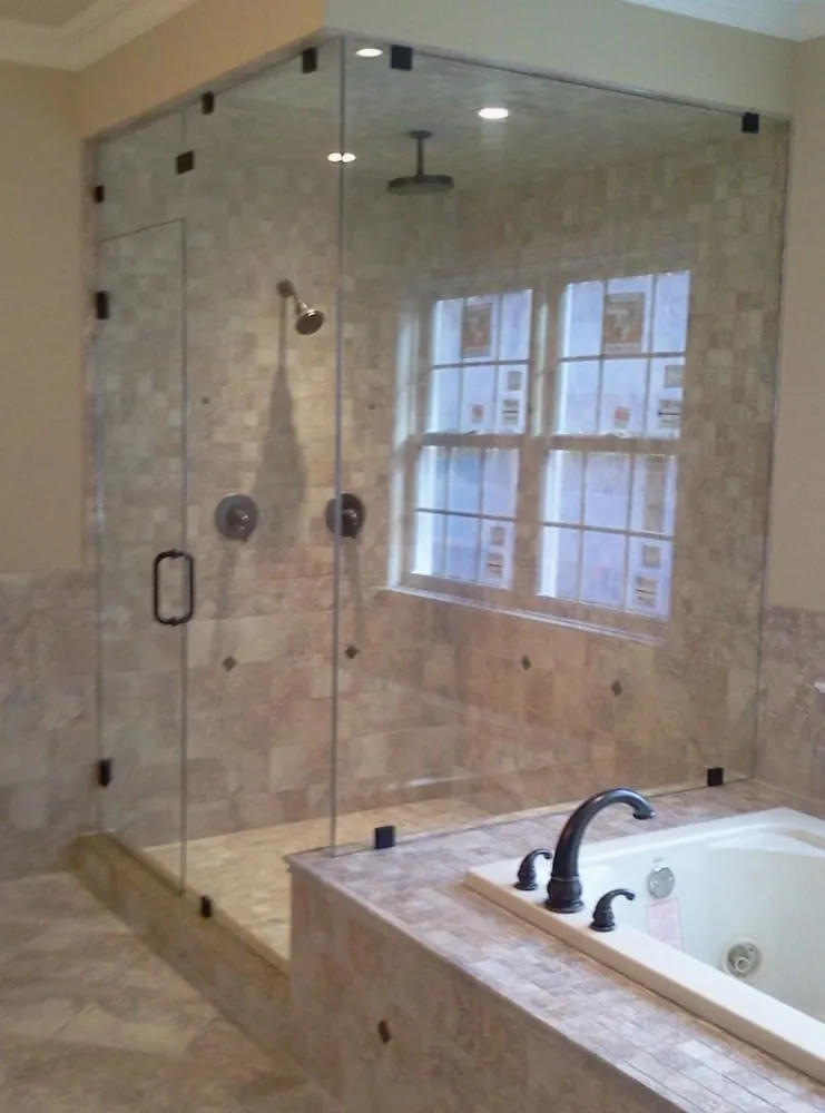 Large glass-enclosed shower with beige travertine tile, rain head and bronze fixtures beside a tiled jetted tub deck.
