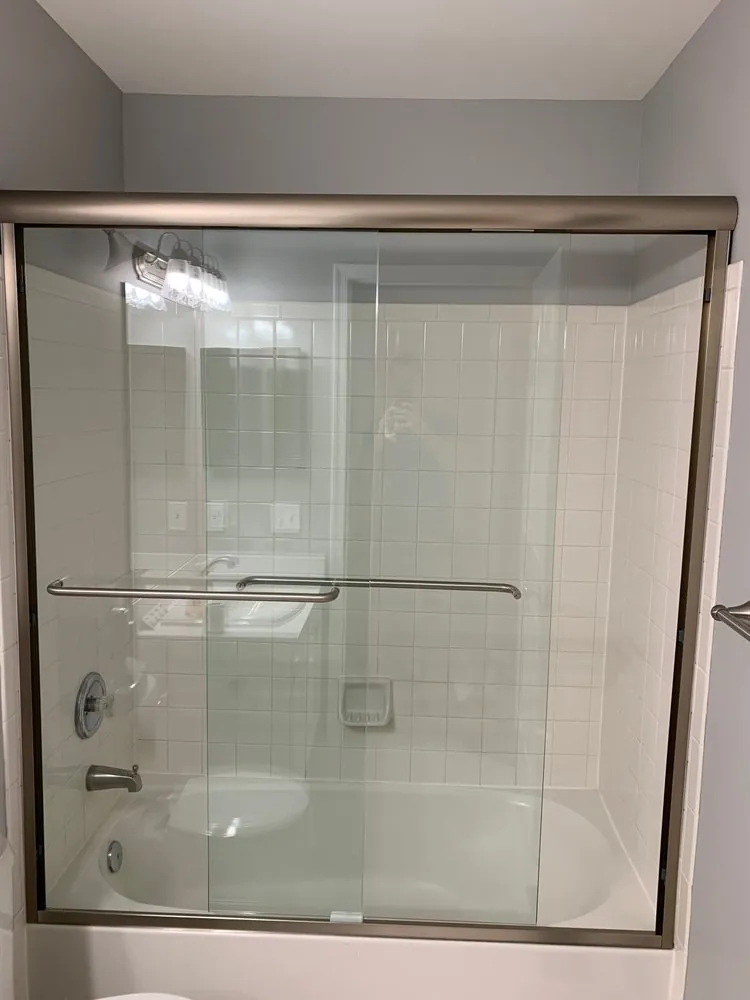 Bathtub with bypass sliding glass doors and brushed nickel frame, white square tile surround and chrome valve.