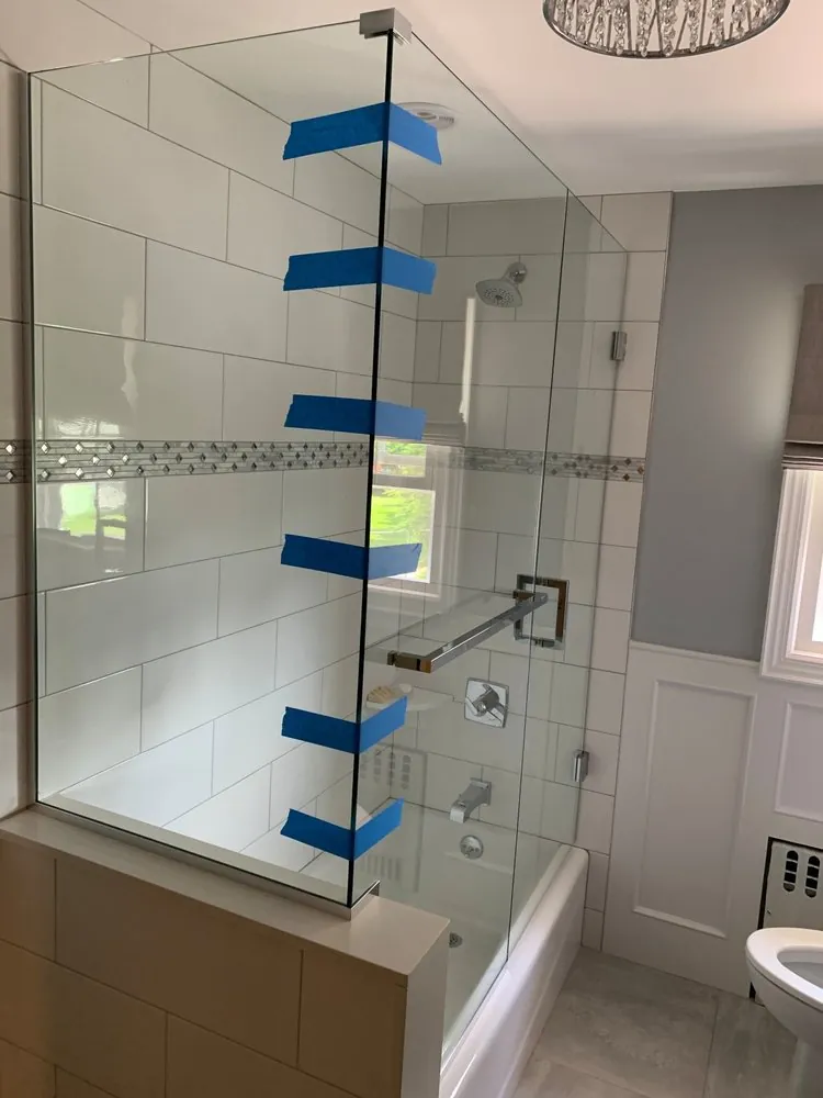 Fixed glass panel over a tub on a tiled knee wall, large white wall tile with diamond mosaic band and white wainscoting.