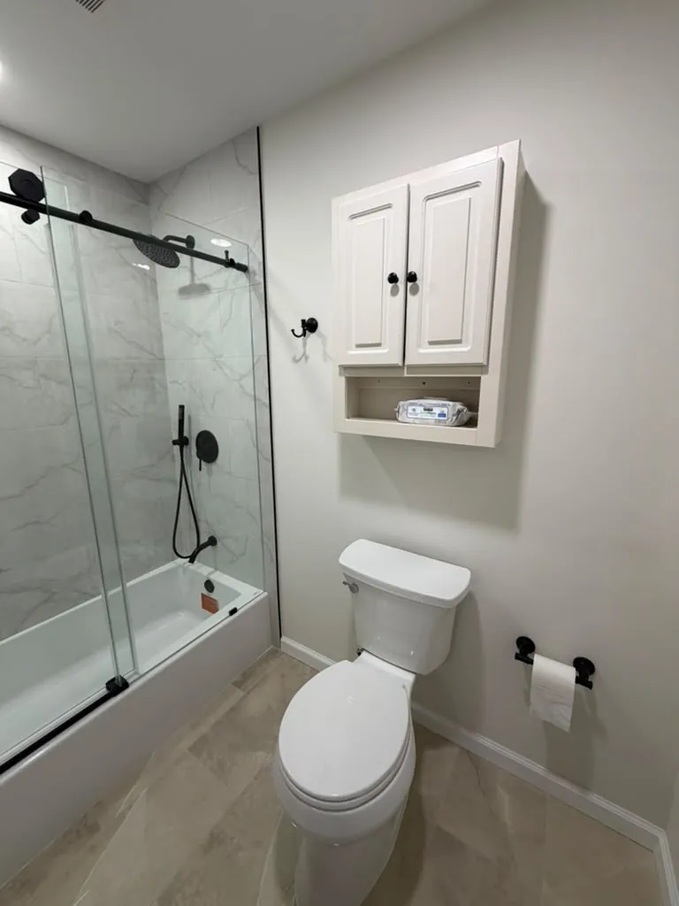 Bathroom with white marble-look tile tub surround, black sliding glass door and fixtures, and a white wall cabinet.