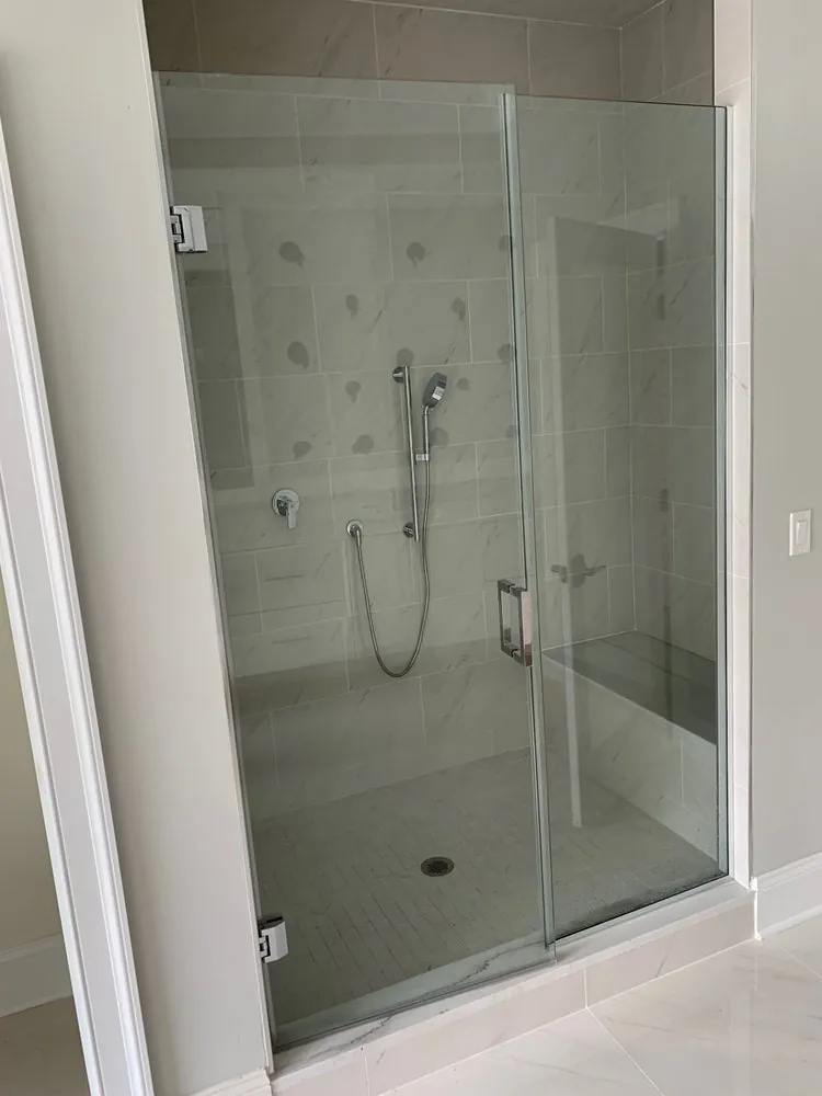 Frameless glass walk-in shower with white marble-look porcelain, chrome hand shower on slide bar and a tiled bench.