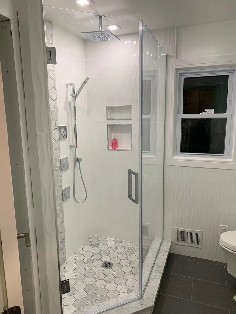 Frameless glass shower with white wave tile, marble hex floor and accent strip, body jets, two niches and rain head.
