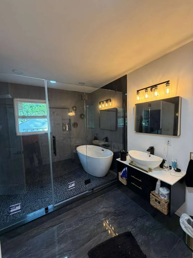 Glass-enclosed shower and freestanding tub on a pebble floor, dark marble tile and a floating vessel sink vanity.