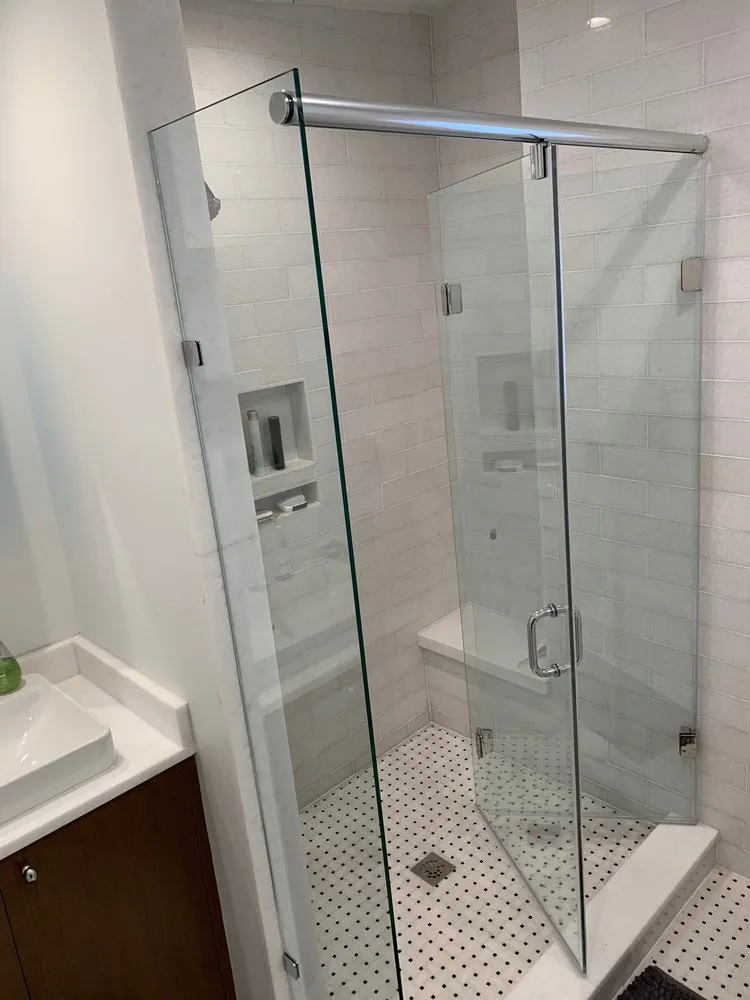 Frameless glass shower with header bar, white stone subway tile, bench, niches and black-and-white dot mosaic floor.