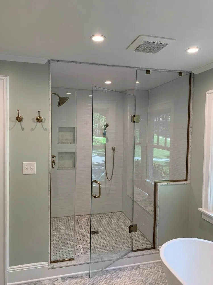 Glass shower with brass hinges and handle, white subway tile, two niches, marble basketweave floor and a freestanding tub.