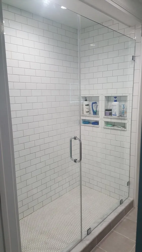Glass walk-in shower with white subway tile, two recessed niches, white penny tile floor and marble curb.