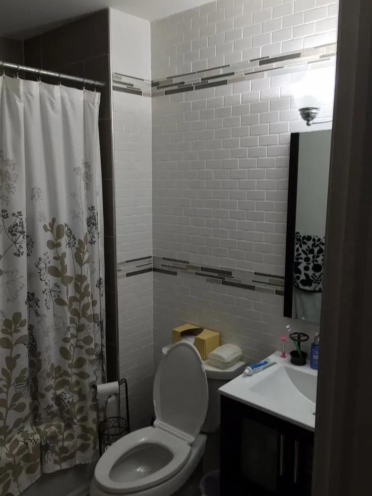 Small bathroom with white subway tile walls, gray glass tile bands, dark vanity with white top, mirror and toilet.