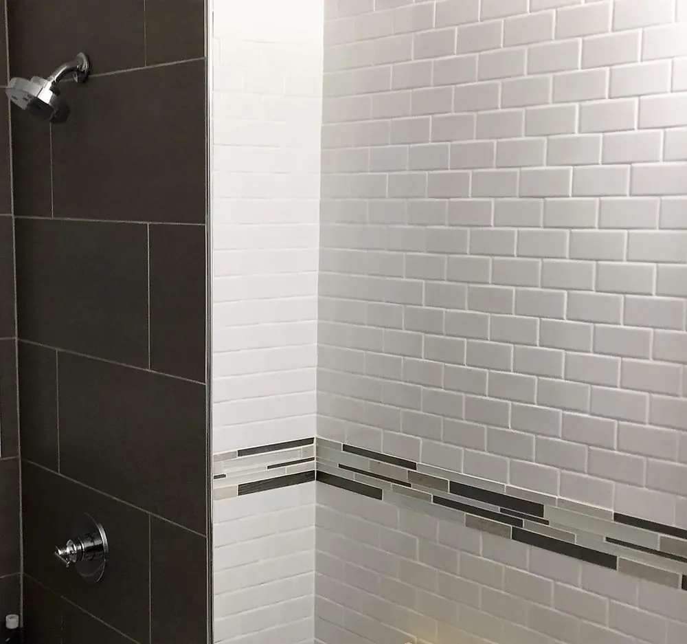 Shower with dark gray large tile on one wall and white subway tile with a glass mosaic border.