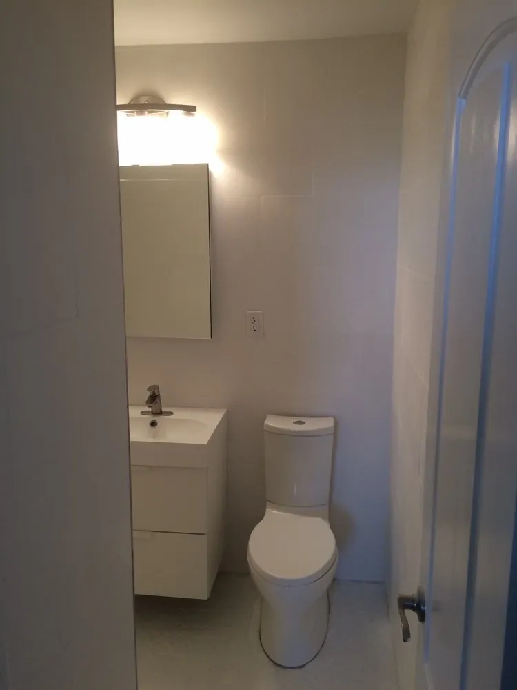 Small bathroom with white wall tile, white floating vanity with drawers, mirrored cabinet, vanity light and two-piece toilet.