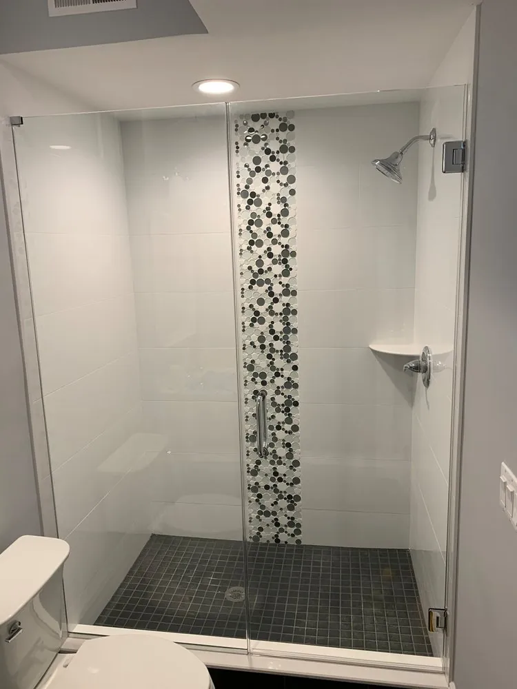 Glass shower with white wall tile, a vertical bubble mosaic strip and dark gray square tile floor.