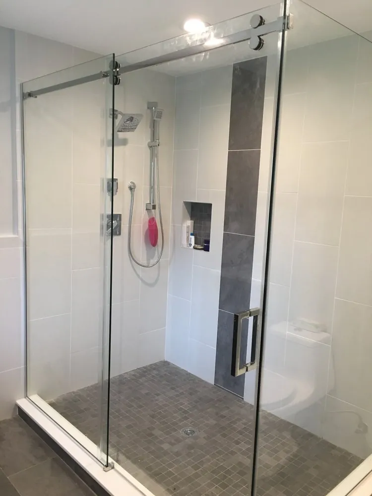 Glass shower with sliding door, large white wall tile, a vertical gray tile stripe, recessed niche and gray mosaic floor.