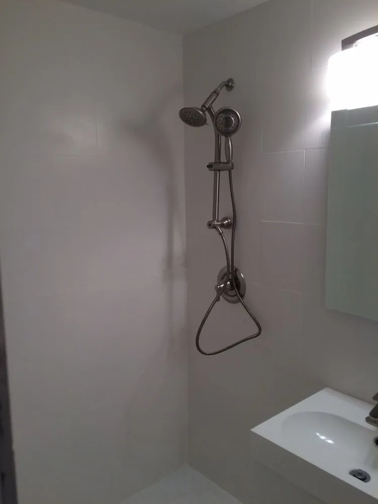 Shower area with large white wall tile, brushed nickel shower column with dual heads and a white wall-mounted sink.