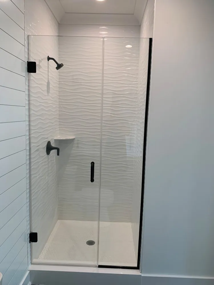 Walk-in shower with white wavy wall tile, white penny tile floor, glass door and matte black fixtures beside shiplap walls.