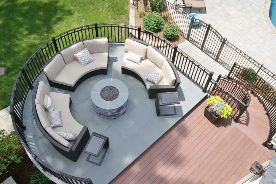 Overhead view of a curved deck with bluestone fire pit area, curved sofas, brown composite boards and black railing.