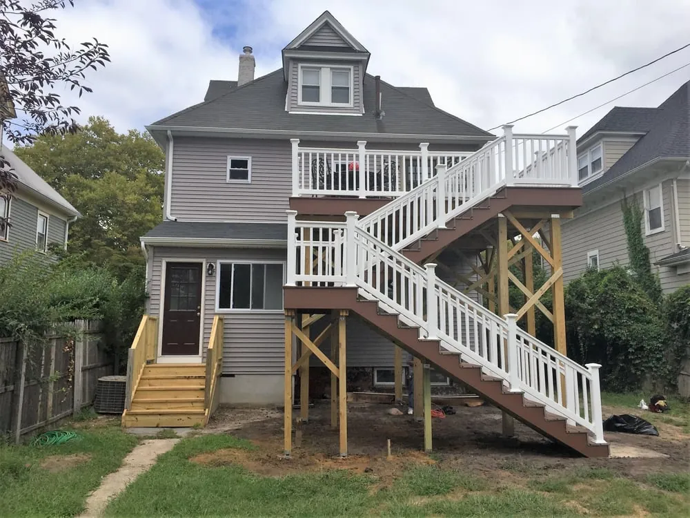 Two-level rear deck with white railings, brown stair treads and a pressure-treated support frame on a gray house.