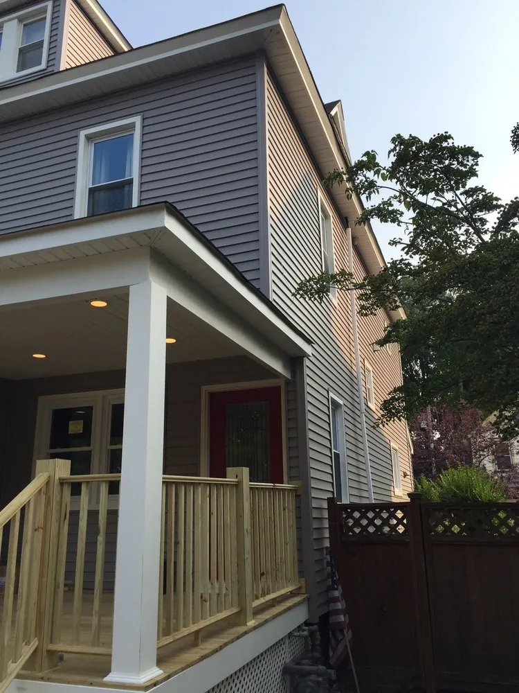 Side view of a covered front porch with a white column, recessed ceiling lights and pressure-treated wood railing.