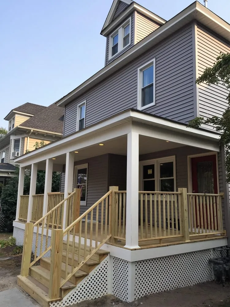 Finished covered front porch with white columns, recessed lights, wood railings and steps and white lattice skirting.