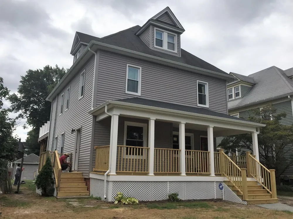 Gray sided foursquare house with a new covered front porch, white columns, wood railings and side entry stairs.