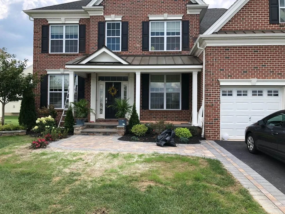 Tan paver walkway and stone porch steps in front of a red brick colonial with a covered entry and fresh plantings.