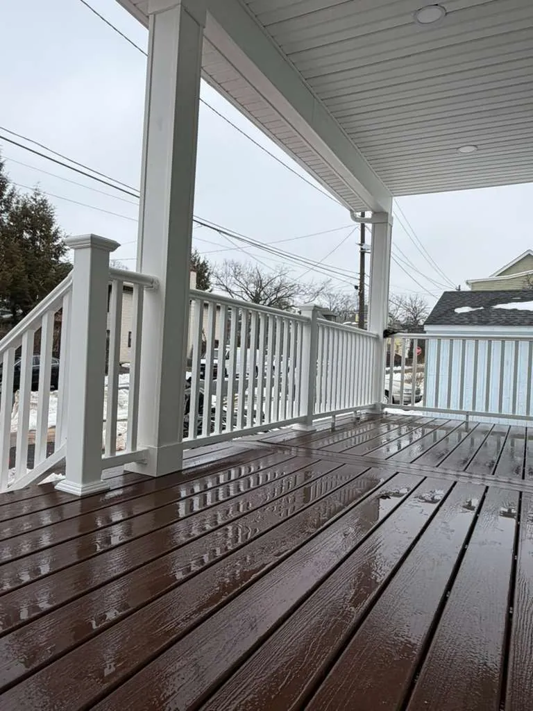 Covered front porch with brown composite decking, white vinyl railings, square columns and a white soffit ceiling.