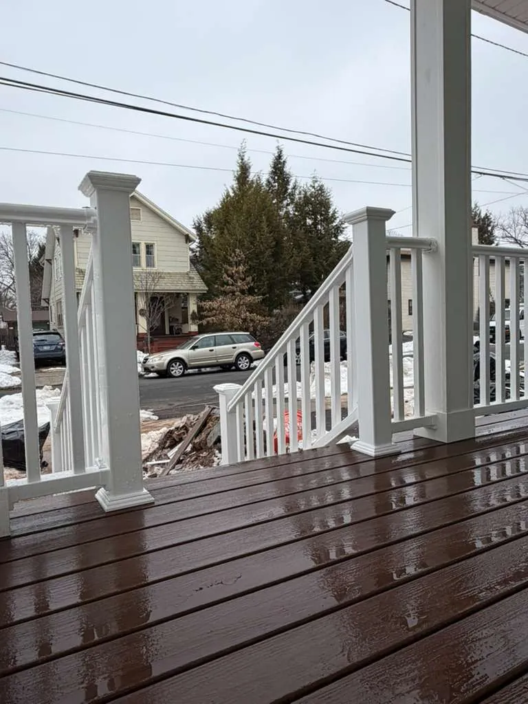Brown composite porch floor with white vinyl railings and stair rail leading down to the front walk.