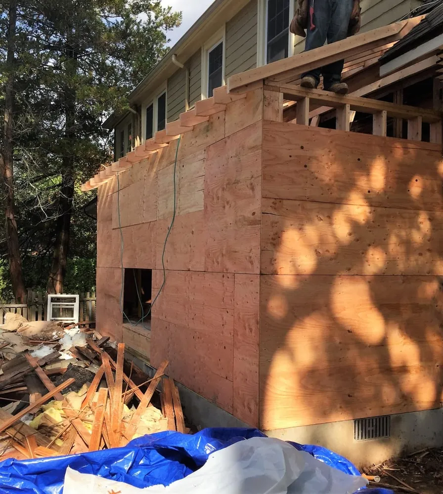 Addition walls sheathed in plywood with new roof rafters going up and a pile of demolition debris beside it.