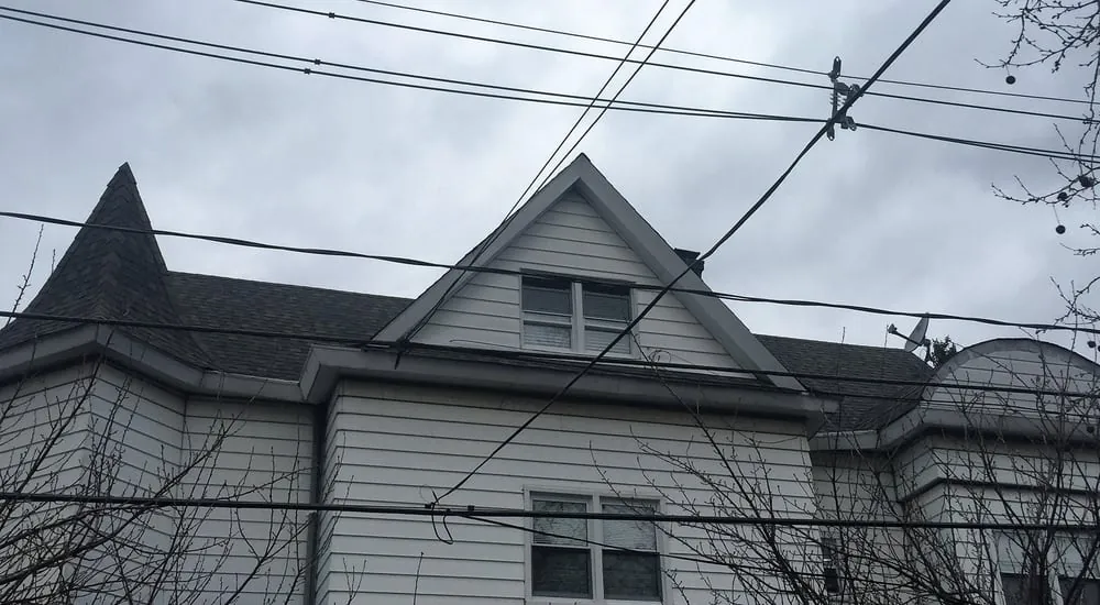 Dark gray shingle roof with a pointed turret and front gable over white siding, crossed by overhead power lines.