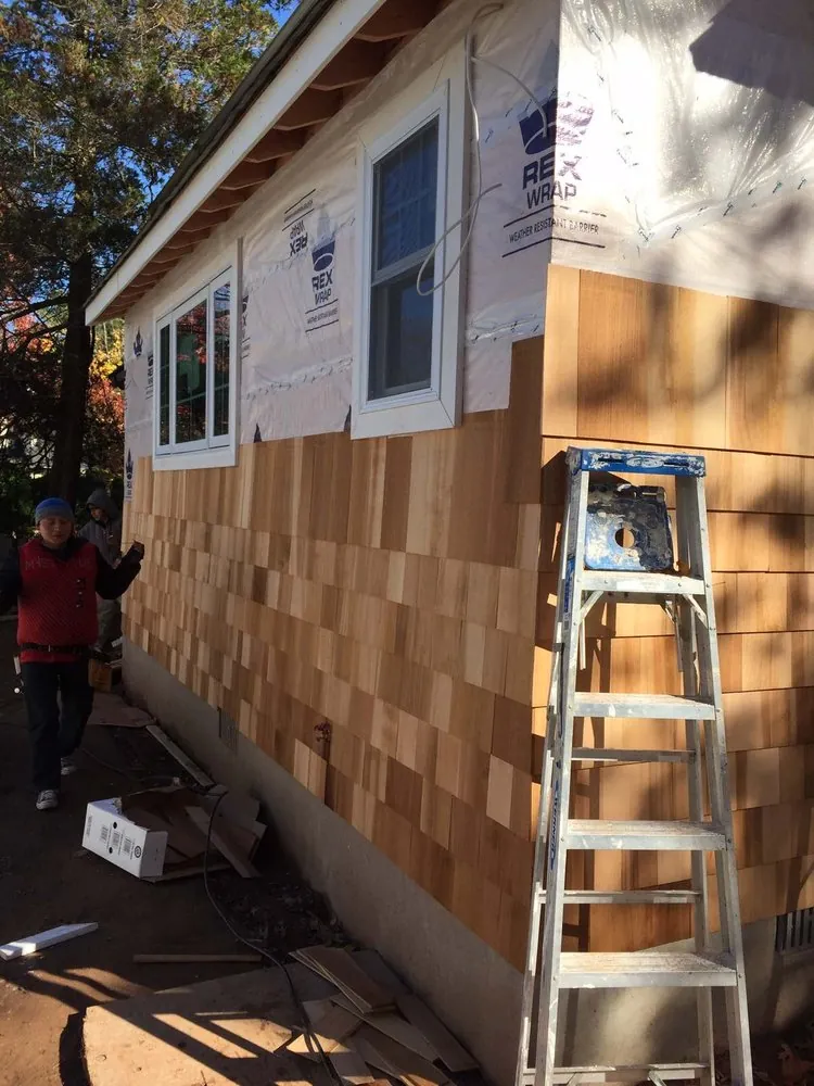 Cedar shake siding being installed over house wrap on an addition with new white windows and a ladder.