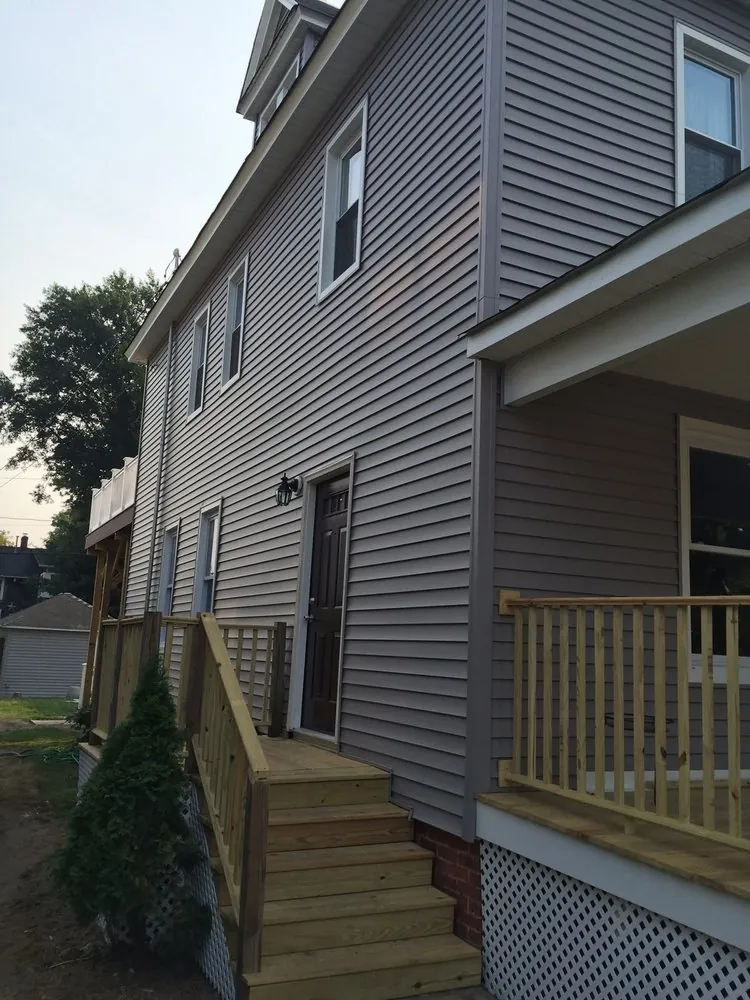 Side of a three-story house with new gray vinyl siding, white windows and a pressure-treated side entry stair.