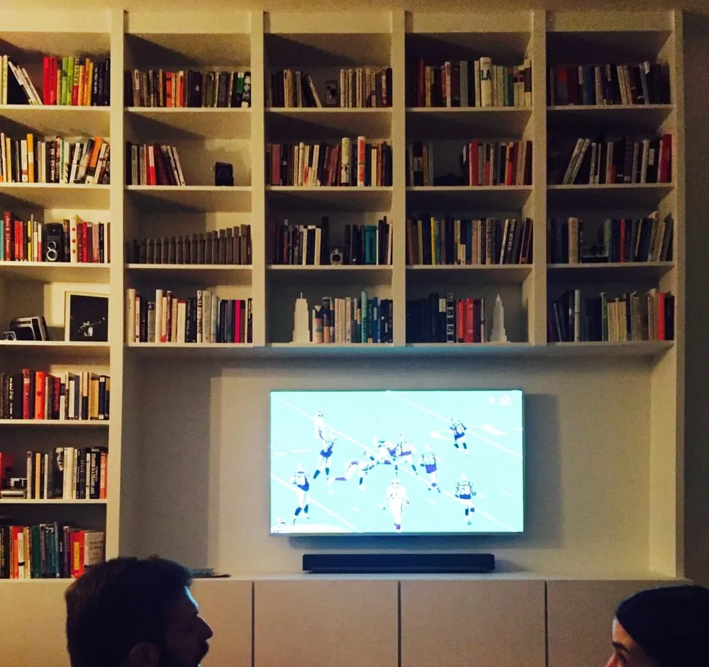 Floor-to-ceiling white built-in bookshelves filled with books around a wall-mounted TV over low cabinets.